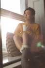 Удумлива жінка має каву біля вікна вдома — стокове фото
