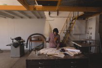 Artigiana donna che lavora con cianografie alla scrivania in laboratorio . — Foto stock