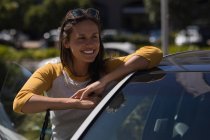 Щаслива жінка стоїть зі своєю машиною в сонячний день — стокове фото