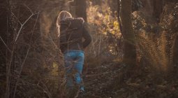 Vista posteriore della donna bionda che cammina nella foresta . — Foto stock