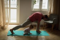 Bebê imitando seu pai enquanto se exercita em casa — Fotografia de Stock
