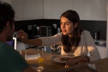 Woman feeding man in kitchen at home — Stock Photo