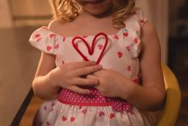 Середня частина дівчини, що тримає прикрасу форми серця вдома — стокове фото