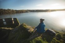 Vista trasera del senderista masculino relajándose cerca del lago en el campo - foto de stock