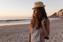 Mujer con sombrero de sol sosteniendo la cámara vintage en la playa al atardecer . - foto de stock
