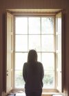 Rückansicht einer Frau, die zu Hause durch das Fenster schaut — Stockfoto