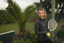 Femme réfléchie tenant raquette et balle de tennis dans le court de tennis — Photo de stock