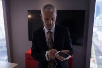 Hombre de negocios enchufe auriculares en el teléfono inteligente en una habitación de hotel - foto de stock