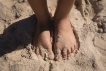 Baixa seção de criança em pé na areia na praia em um dia ensolarado — Fotografia de Stock