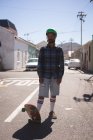 Uomo in piedi con skateboard in strada alla luce del sole — Foto stock