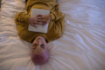 Vista aerea di giovane donna con capelli rosa che dorme con tablet digitale sul letto . — Foto stock