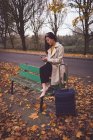 Businesswoman using mobile phone while sitting on bench during autumn — Stock Photo