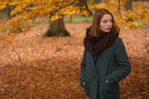 Жінка стоїть з руками в кишені в парку восени — стокове фото