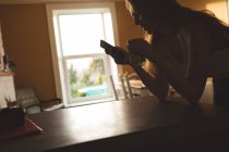 Женщина, пользующаяся мобильным телефоном, пьет кофе дома — стоковое фото