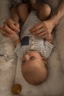 Primo piano del piccolo bambino carino sdraiato sul letto che tiene le mani della madre a casa — Foto stock