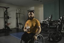 Молодий інвалідний чоловік на інвалідному візку з пляшкою води в тренажерному залі — стокове фото