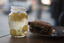 Primer plano de tarro de té de limón con alimentos envueltos en el plato en la cafetería - foto de stock
