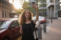 Mulher bonita tomando selfie com telefone celular em um dia ensolarado, segurando café — Fotografia de Stock