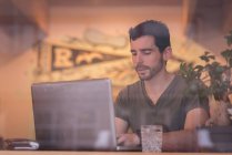 Mid adult man using laptop in cafe behind window. — Stock Photo