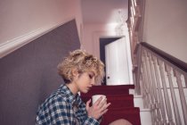 Young woman shaving coffee on staircase at home — Stock Photo