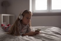 Дівчина слухає музику на мобільному телефоні з навушниками в спальні вдома — стокове фото
