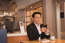 Businessman using smartphone while having coffee in coffee shop — Stock Photo