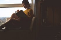 Frau liest zu Hause am Fenster ein Buch — Stockfoto