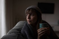 Nachdenkliche Frau mit Tasse Kaffee im Wohnzimmer. — Stockfoto