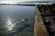 Женщина плавает в бассейне на пляже под солнечным светом — стоковое фото