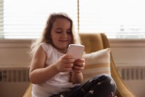 Menina sorrindo usando telefone celular em casa — Fotografia de Stock