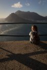 Rückansicht einer rothaarigen Frau, die an einem Aussichtspunkt im Sonnenlicht sitzt — Stockfoto