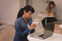 Ejecutivo femenino usando el ordenador portátil mientras toma café en la oficina creativa - foto de stock