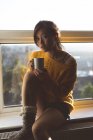 Женщина пьет кофе у окна дома — стоковое фото