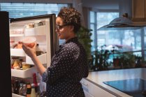 Feliz joven embarazada de pie cerca del refrigerador en busca de comida en la cocina en casa - foto de stock