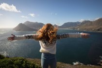 Visão traseira da mulher com os braços estendidos em pé perto do lago — Fotografia de Stock
