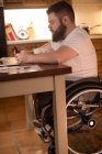 Homme handicapé utilisant un téléphone portable tout en travaillant sur un ordinateur portable à la maison — Photo de stock