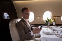 Uomo d'affari attento utilizzando il telefono cellulare in jet privato — Foto stock