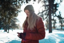 Frau in Winterkleidung mit Handy an einem sonnigen Tag — Stockfoto