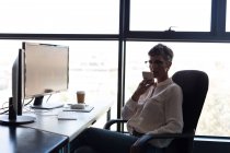 Зріла бізнес-леді розмовляє по мобільному телефону, маючи каву в офісі — стокове фото