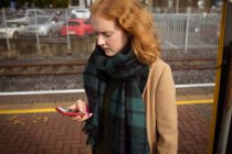 Giovane donna che utilizza il suo telefono cellulare alla piattaforma ferroviaria in una giornata di sole — Foto stock