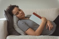 Femme dormant tout en tenant le livre dans la main sur le canapé — Photo de stock