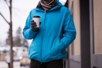 Mid section of man holding disposable coffee cup on sidewalk. — Stock Photo