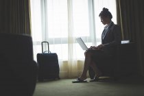Бізнес-леді, використовуючи ноутбук, сидячи на кріслі в готельному номері — стокове фото