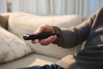 Mid section of man changing channel with remote control at home — Stock Photo
