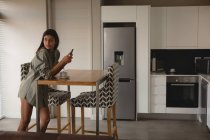 Mujer usando teléfono móvil en la cocina en casa - foto de stock