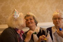 Senior woman kissing her senior friend during birthday celebration at home — Stock Photo
