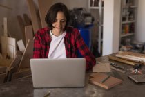 Young craftswoman using laptop at desk in workshop. — Stock Photo
