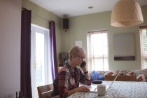 Зрілі жінки говорять на мобільному телефоні під час використання ноутбука на дому — стокове фото