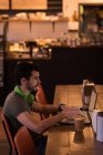 Середній дорослий чоловік використовує ноутбук у кафе, вид збоку . — стокове фото
