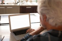 Hombre mayor usando el ordenador portátil en la cocina en casa - foto de stock